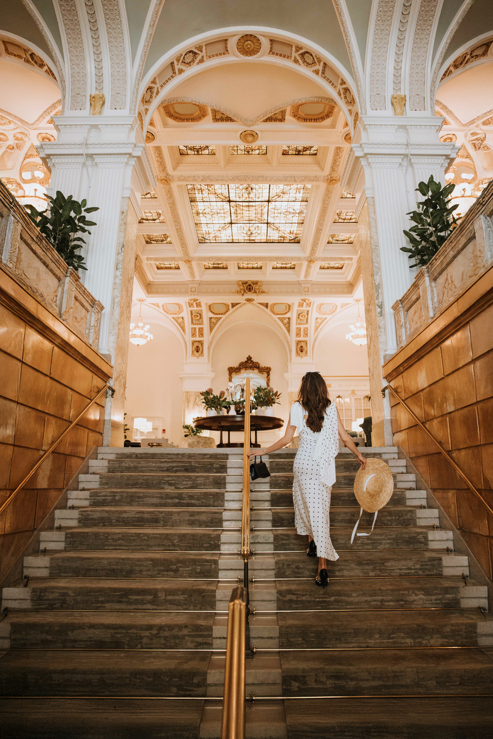 woman walking up the stairs holding a sunhat