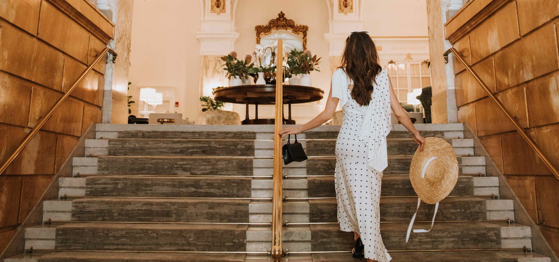 woman walking up the stairs holding a sunhat