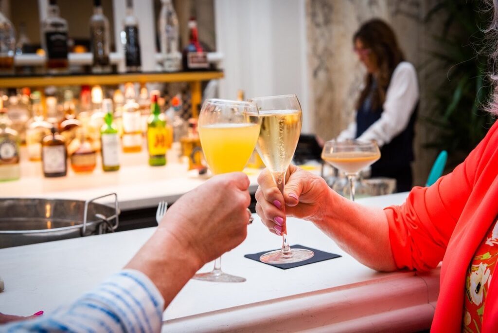 Two women clink mimosas served in champagne flutes together while seated at a luxurious nashville hotel bar.
