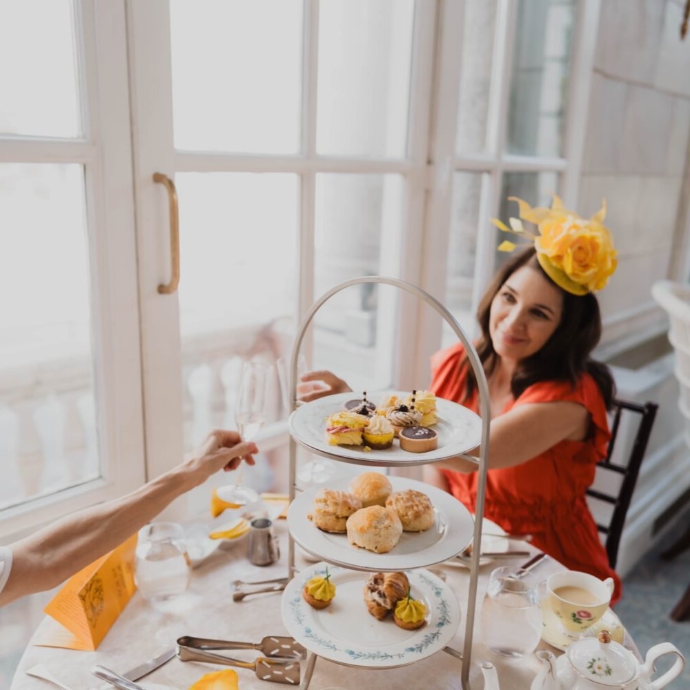 A woman in a red dress and yellow rose fascinator enjoys a three-tiered afternoon tea at the Hermitage Hotel's Yellow Rose Tea, honoring the Women's Suffrage Movement in Nashville, TN.