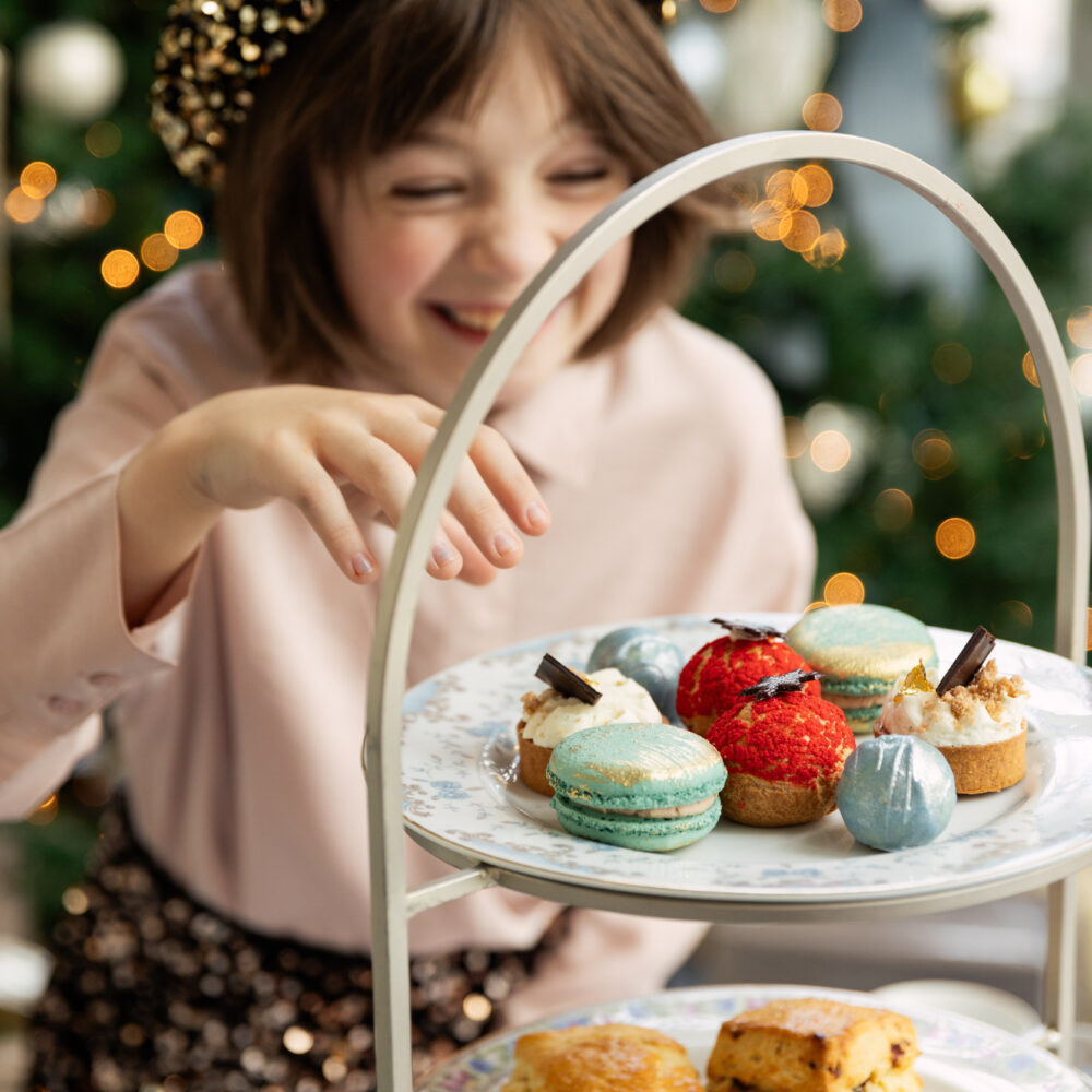 Child reaching for colorful pastries on an afternoon tea stand.
