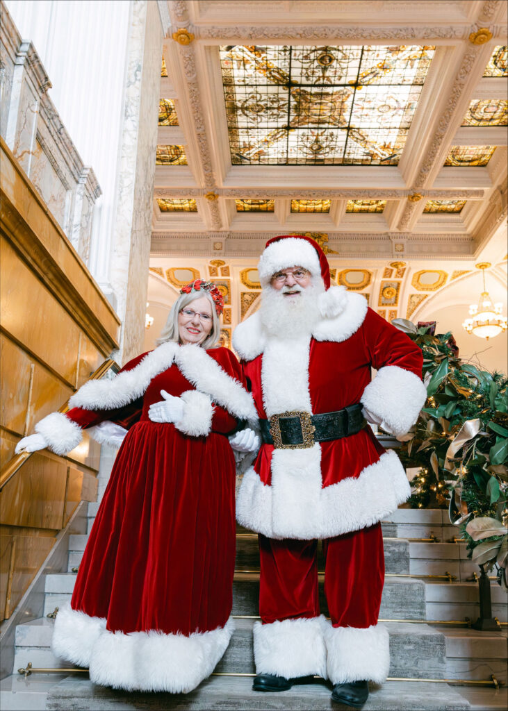 Santa and Mrs. Claus standing on decorated hotel staircase.