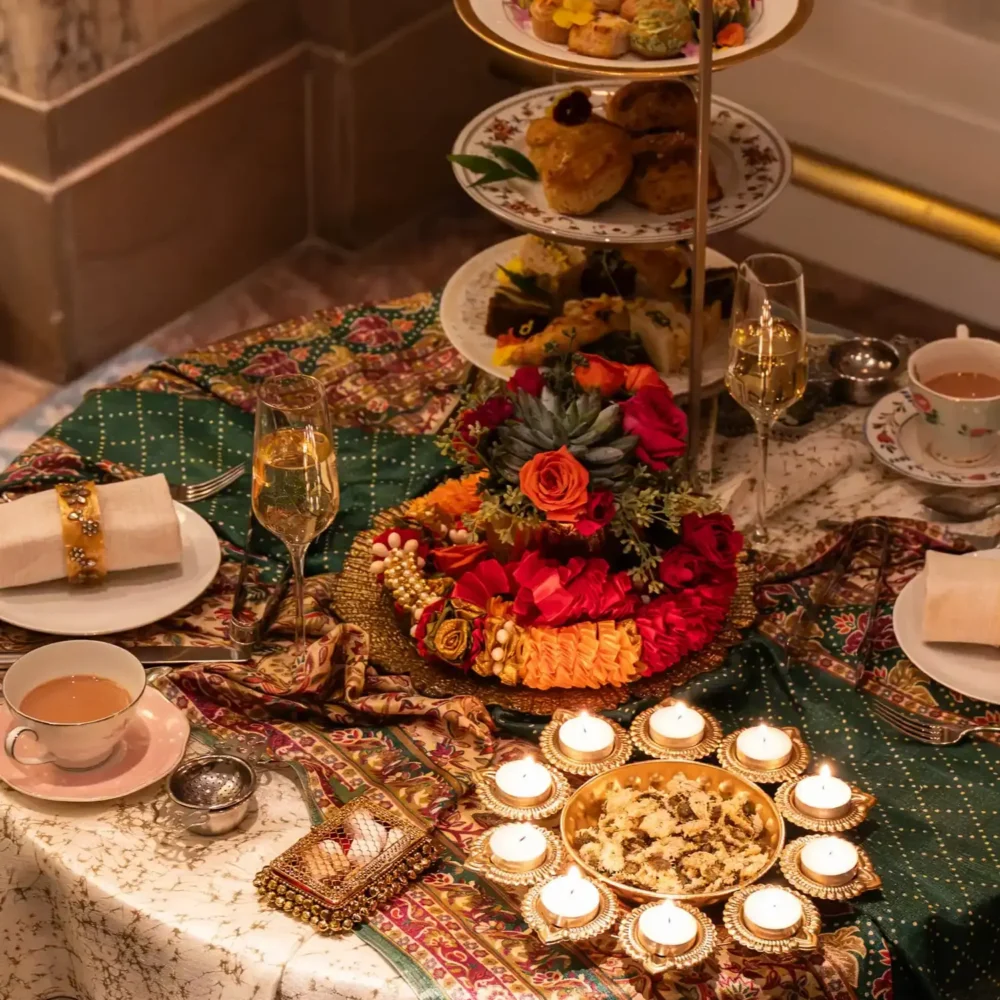 Diwali-themed afternoon tea table with tiered pastries, flowers, tea, champagne, and lit candles.