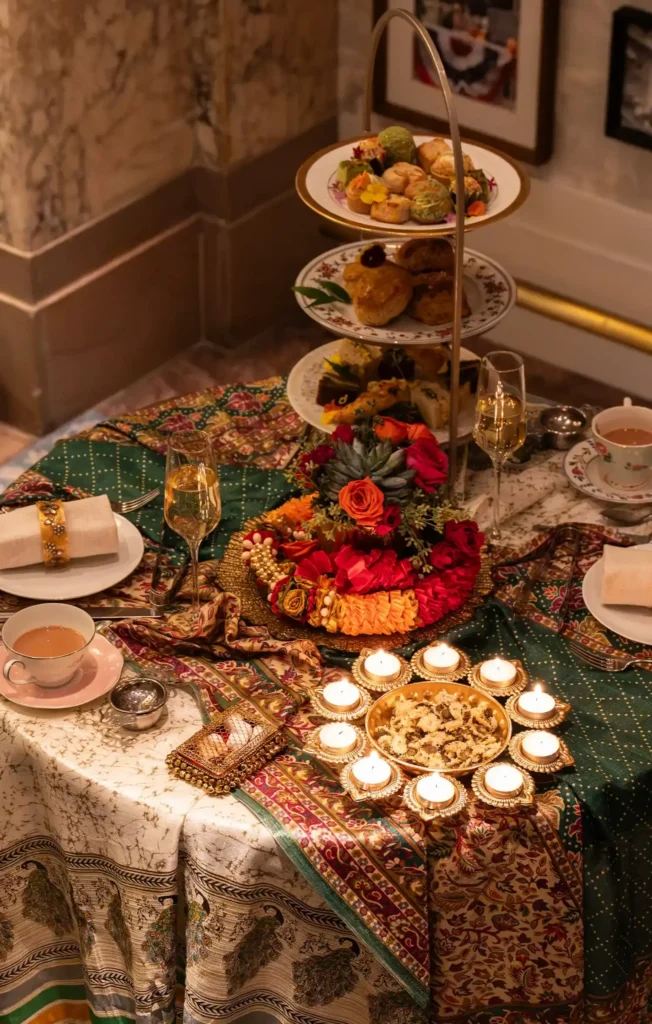 Diwali-themed afternoon tea table with tiered pastries, flowers, tea, champagne, and lit candles.