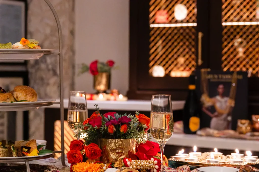 Afternoon tea display with champagne, red and orange flowers, candles, and tiered plates of food.