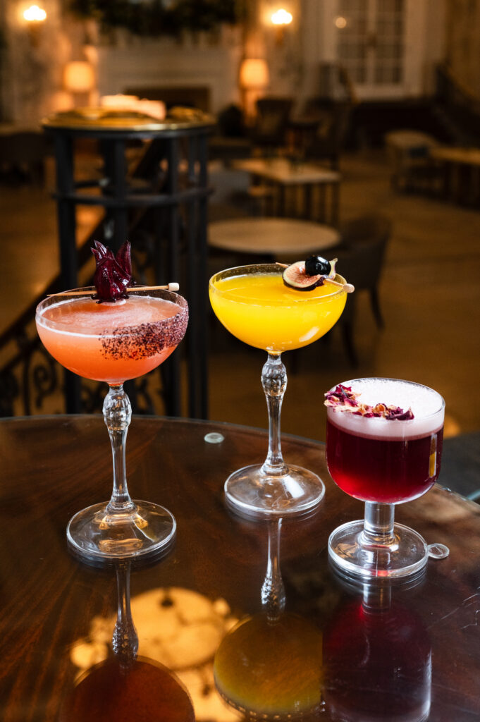 Three colorful drinks with fruit and floral garnishes on a table.
